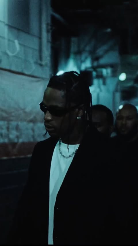 Portrait view of an African American male in a suit and sunglasses, walking towards the camera in an outdoor urban environment.