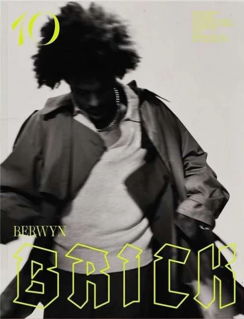 Magazine cover featuring a person in a trench coat with an afro hairstyle, set against a light background with neon yellow text elements.