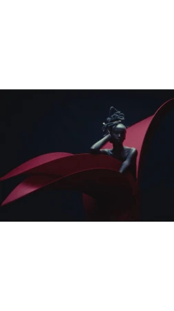 An adult female posing with artistic red fabrics against a dark backdrop in a visually striking beauty or fashion editorial image.