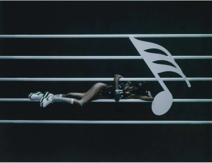 Woman in a bodysuit and sneakers reclines on a musical staff with a large eighth note in this fashion-music crossover scene.