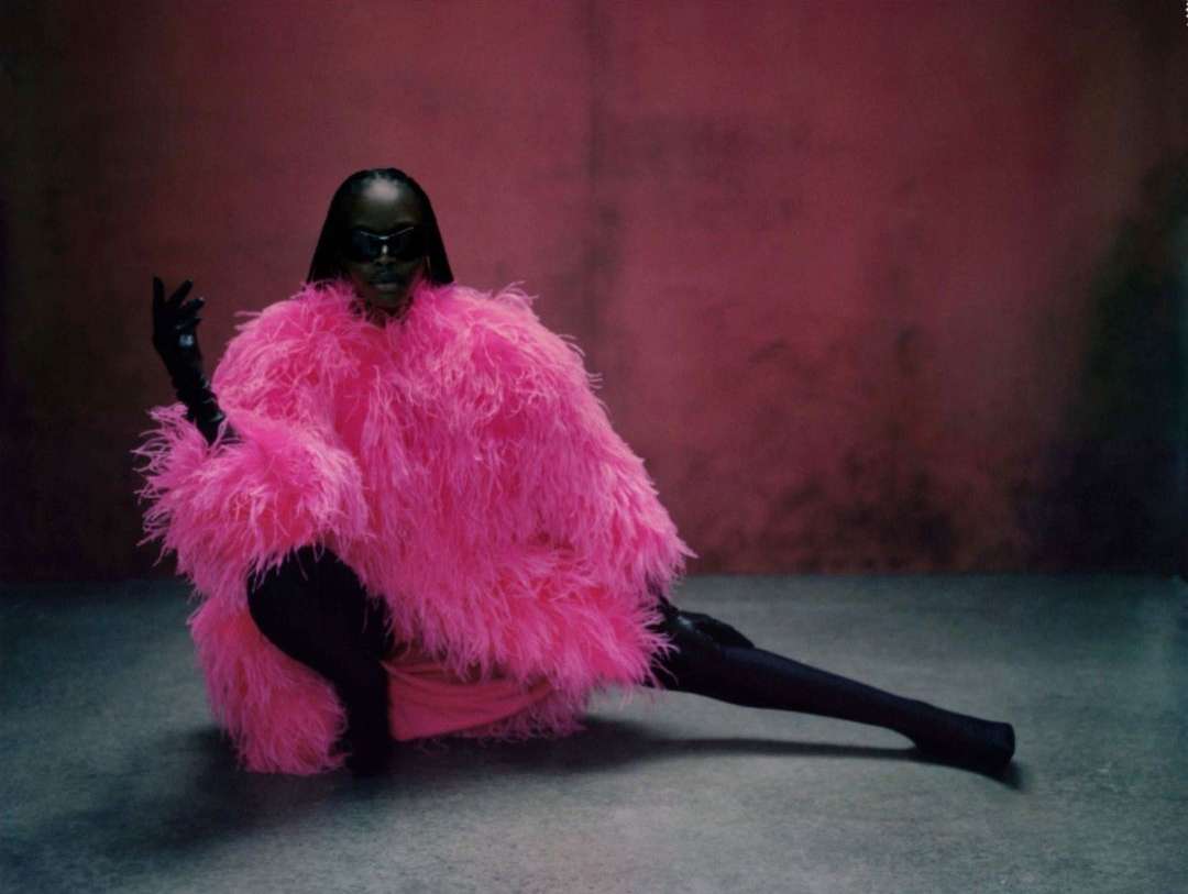 Fashionable adult in striking pink feathered coat poses in studio against pink backdrop, exuding unique style and confidence.