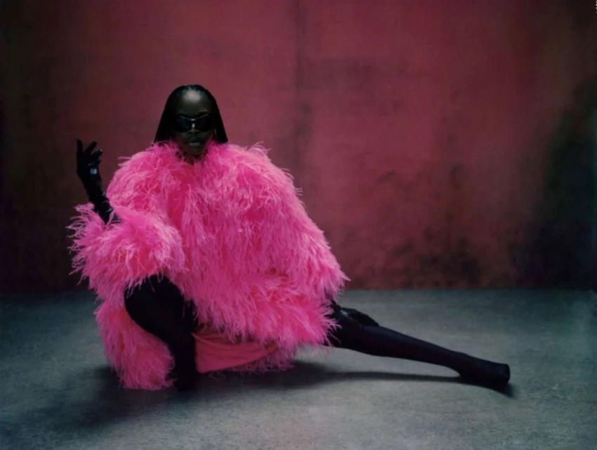 Fashionable adult in striking pink feathered coat poses in studio against pink backdrop, exuding unique style and confidence.