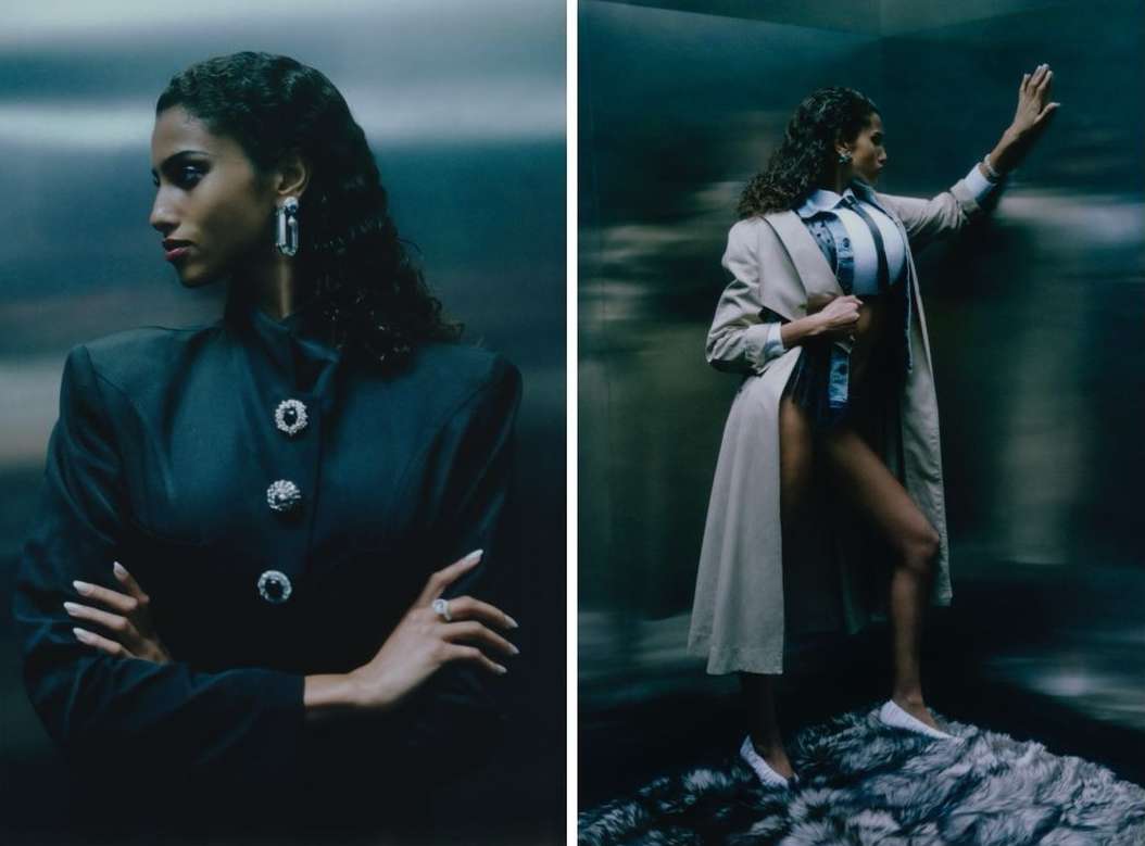 Elegant woman poses in an elevator wearing a dark blazer with jewel buttons and a light trench coat for a high-fashion photoshoot.