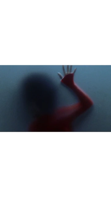 Abstract, blurred image of a person in red clothing with hand pressed against frosted glass, creating a mysterious and obscured view.