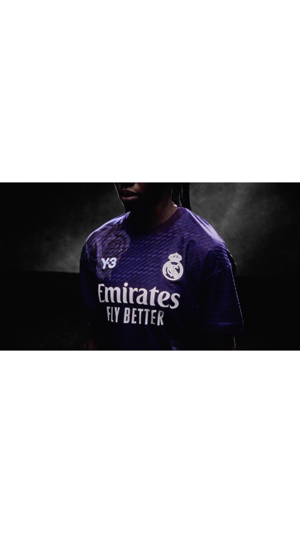 Close-up of a person wearing a purple soccer jersey with a sponsor logo and the Real Madrid emblem against a dark background.