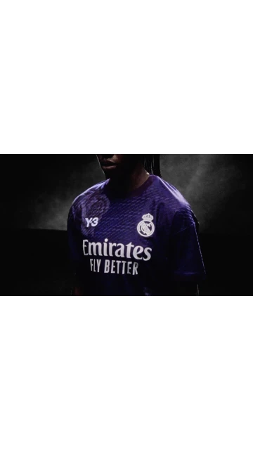 Close-up of a person wearing a purple soccer jersey with a sponsor logo and the Real Madrid emblem against a dark background.
