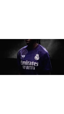Close-up of a person wearing a purple soccer jersey with a sponsor logo and the Real Madrid emblem against a dark background.