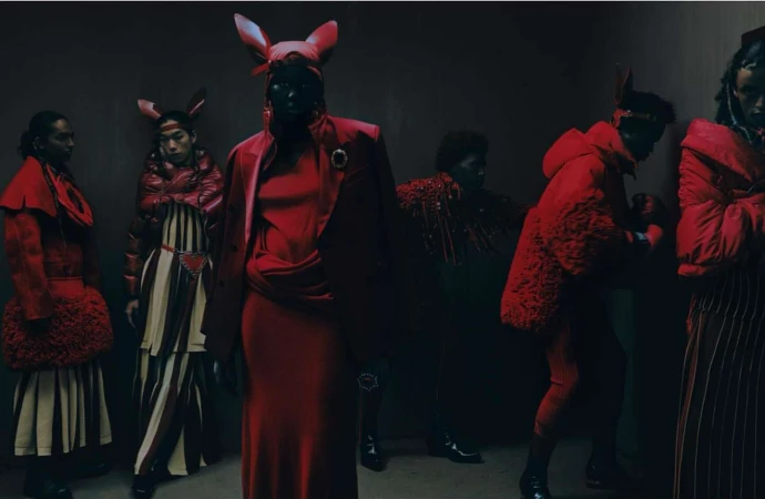 Group of diverse fashion models in red outfits and animal ear headbands pose in a dark indoor setting, presenting a unique editorial style.