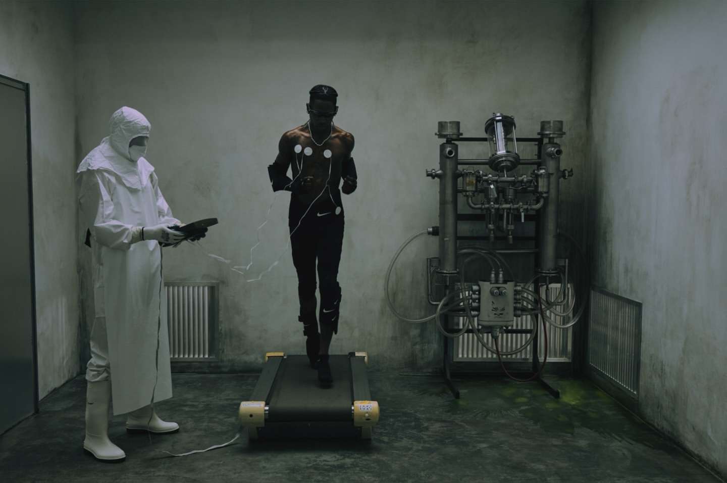 Athletic Black man runs on a treadmill wearing fitness trackers; a scientist in a hazmat suit observes in an indoor clinical setting.