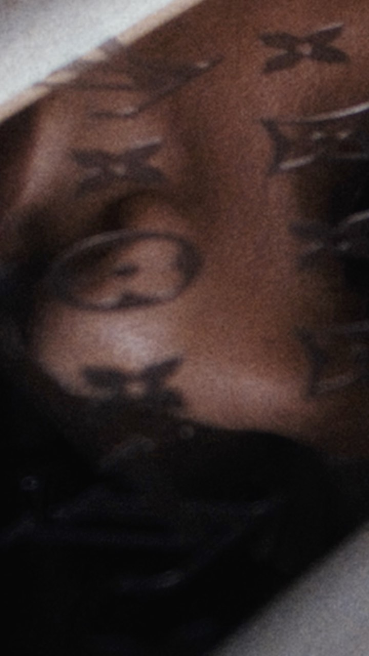 Close-up of a person's shoulder and part of their face, adorned with a designer pattern, set against a dark background.
