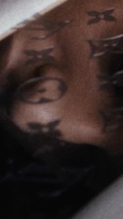 Close-up of a person's shoulder and part of their face, adorned with a designer pattern, set against a dark background.