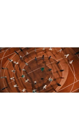 Aerial view of diverse group of people in circular patterns on a brown surface, suggesting unity, community, or planned arrangement.