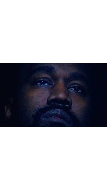 Close-up portrait of a dark-skinned adult male with a beard and mustache looking upward in a dark environment with dramatic lighting.