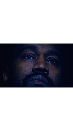 Close-up portrait of a dark-skinned adult male with a beard and mustache looking upward in a dark environment with dramatic lighting.