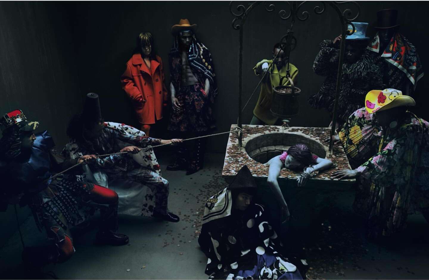 Artistic fashion editorial shot in a dark studio, showcasing a well with people in costume standing and pulling a woman out of it.