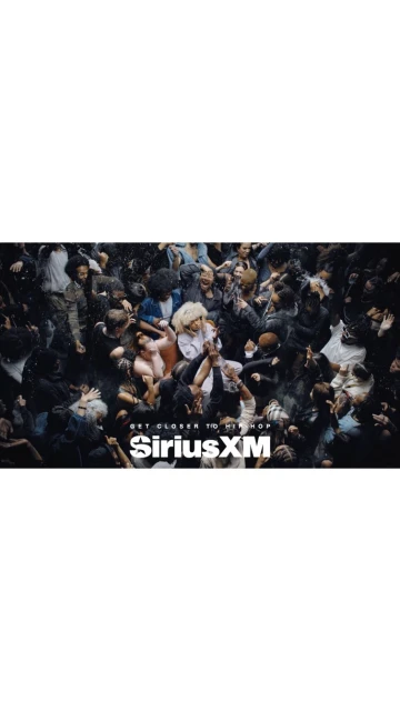 Concert crowd in low light with the SiriusXM logo in the foreground. The angle is high and shows the top of the heads of the crowd.