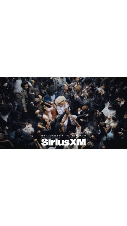 Concert crowd in low light with the SiriusXM logo in the foreground. The angle is high and shows the top of the heads of the crowd.