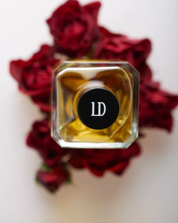 Top-down view of a square glass perfume bottle surrounded by deep red roses against a white background