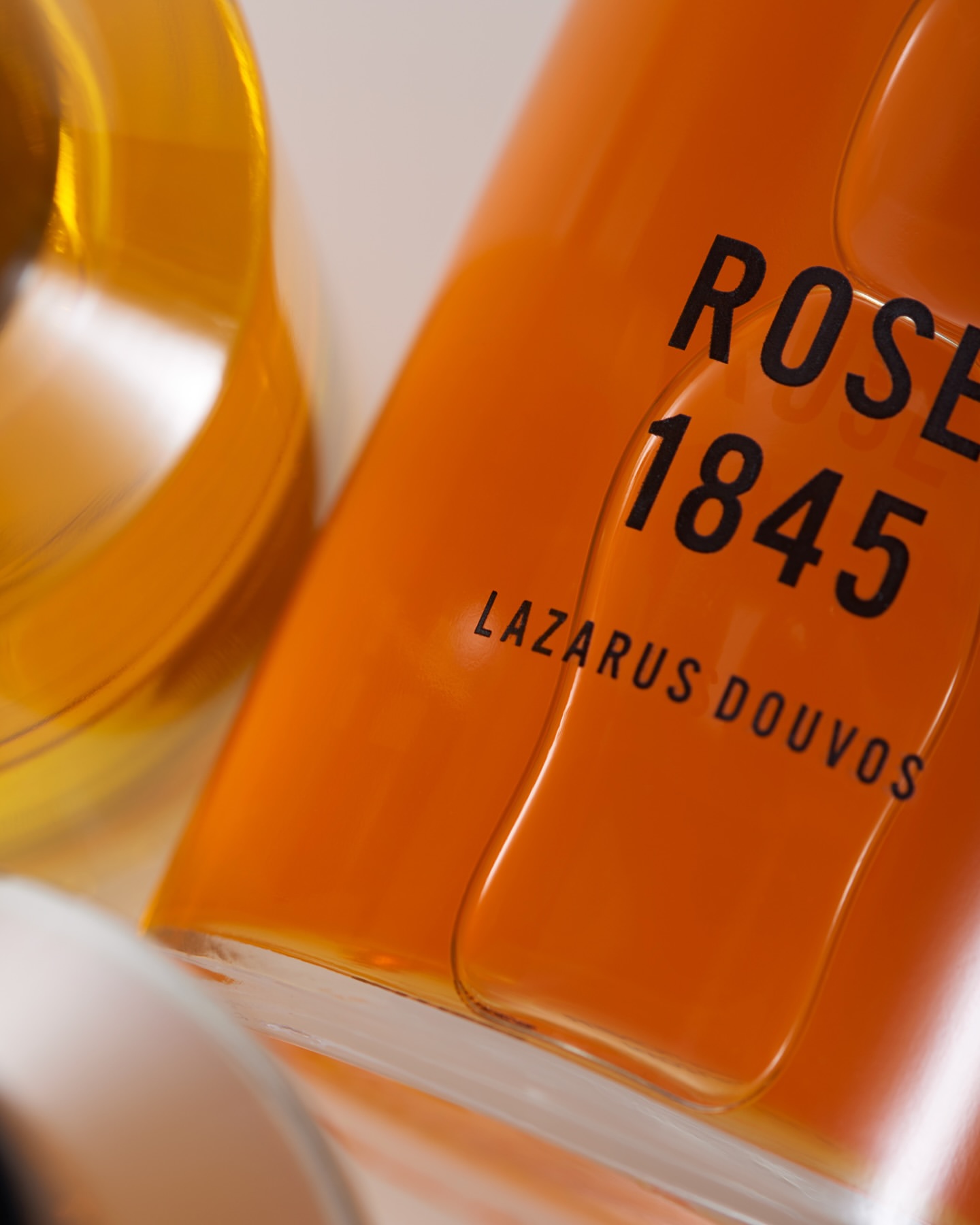 Close-up of an orange glass bottle featuring the text 'ROSE 1845 LAZARUS DOUVOS' in black lettering.