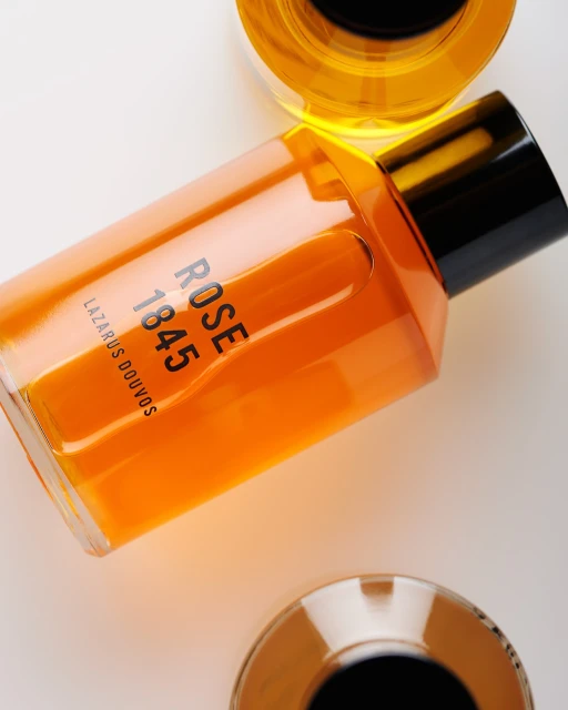 Angular shot of a transparent amber glass perfume bottle with black cap and gold accents against a white backdrop.