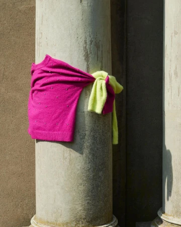 Two sweaters, one hot pink and one chartreuse, tied around a gray concrete column with classical base, outdoor setting.
