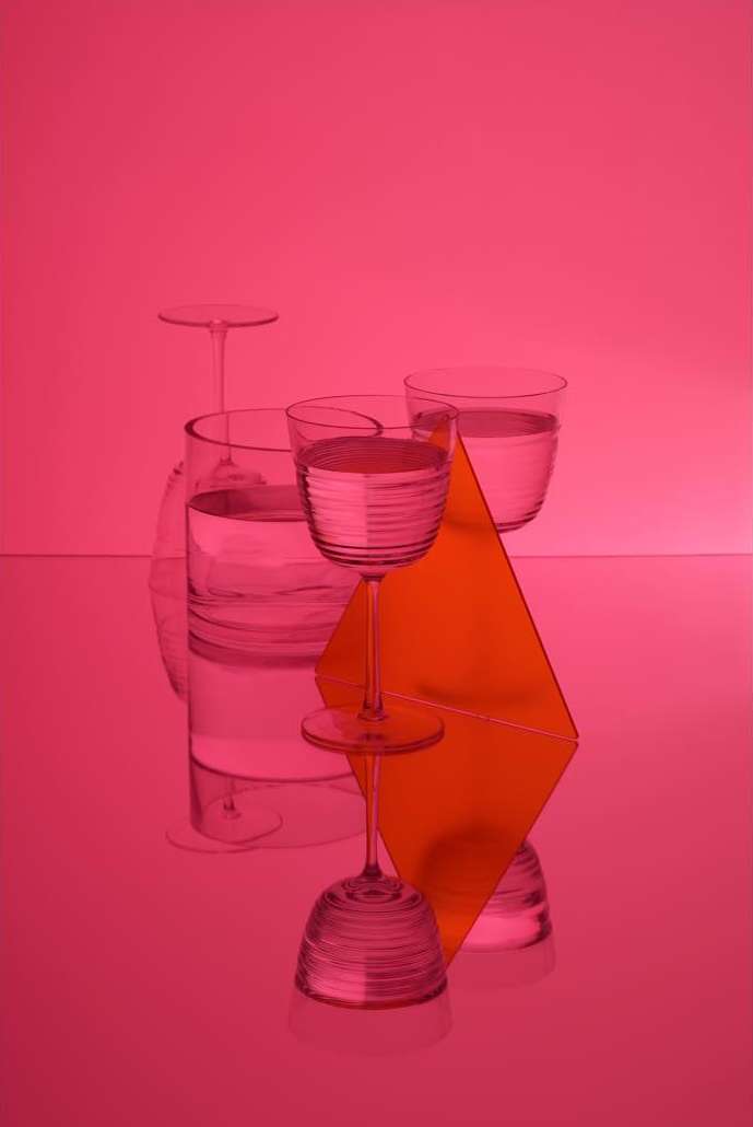 Still life photograph features glasses filled with liquid, in tones of pink and orange, creating an artistic and visually intriguing composition.