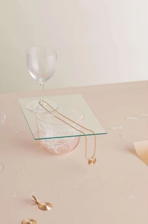 Elegant composition of a gold necklace draped over glassware atop a pink surface, creating a minimalist, high-end jewelry showcase.