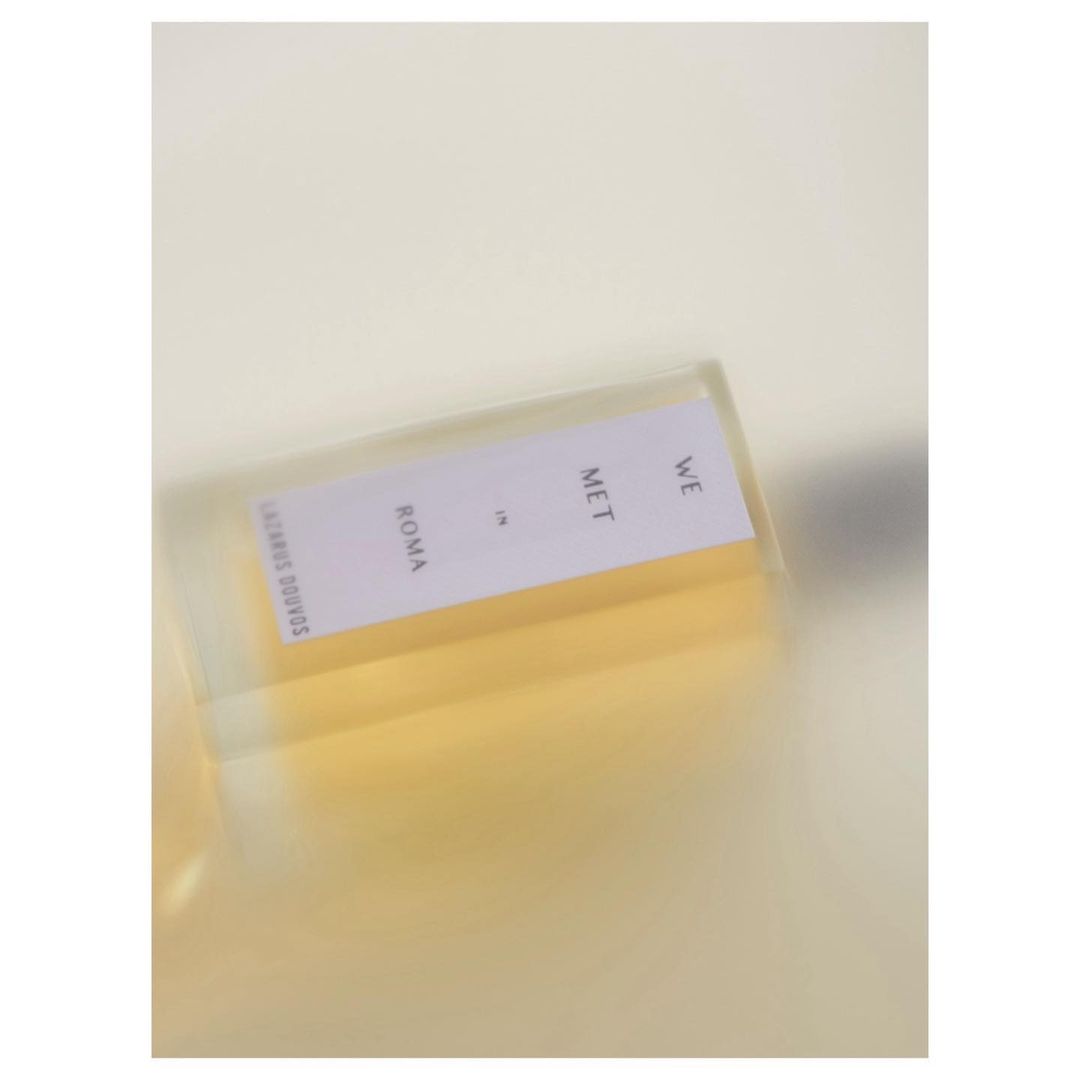 Close-up of a translucent container holding a white card with the text 'WE MET in ROMA' in black lettering against a blurry background.