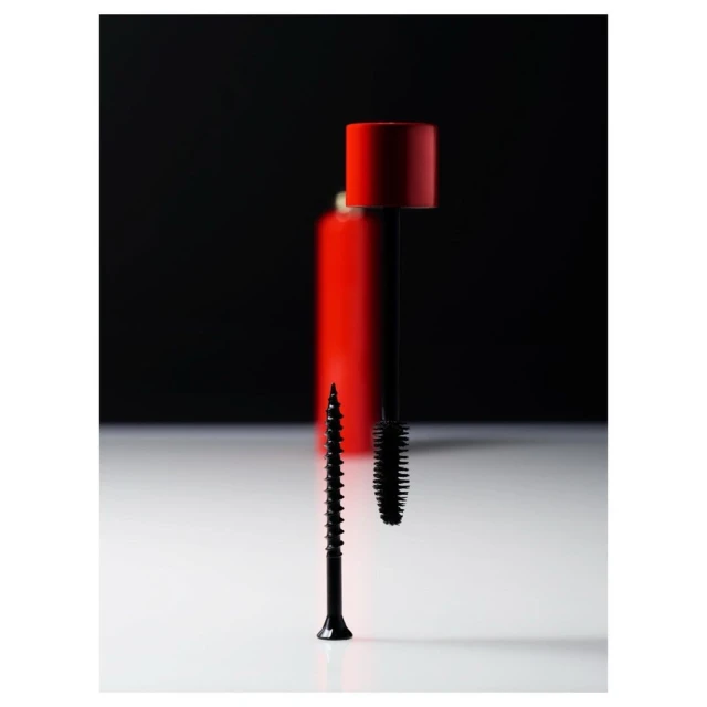 Close-up still life of black mascara brush and a black screw standing on a white surface against a dark background. 