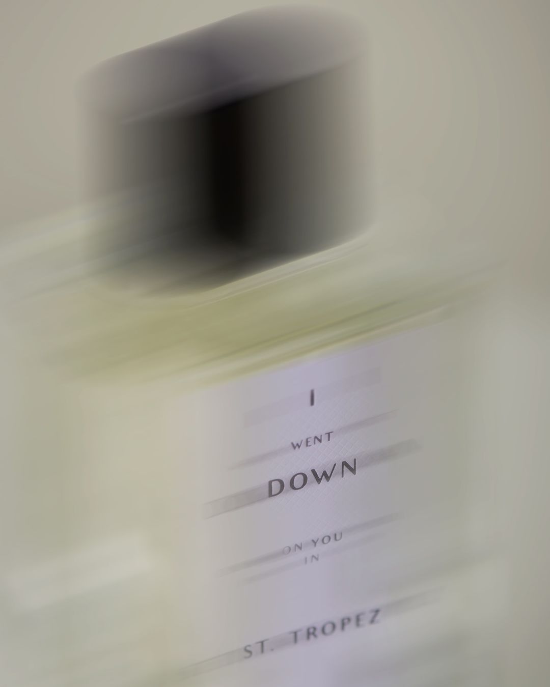 Motion blurred close-up shot of a perfume bottle with printed label against a neutral background by Gabriela Worosz.