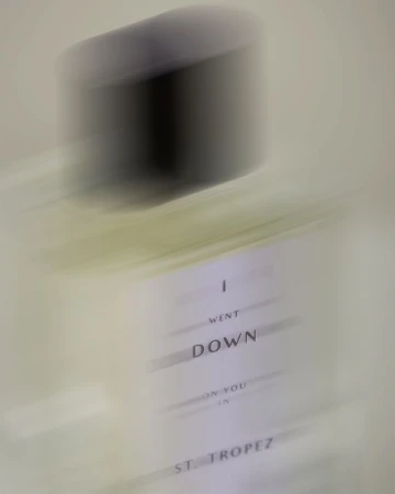 Motion blurred close-up shot of a perfume bottle with printed label against a neutral background by Gabriela Worosz.