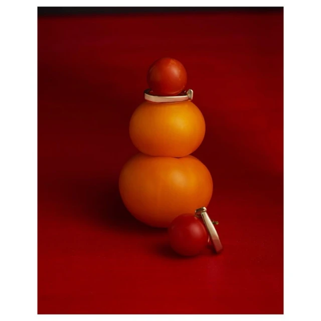 Stack of produce featuring tomatoes and oranges on a red background, product photography, still life.