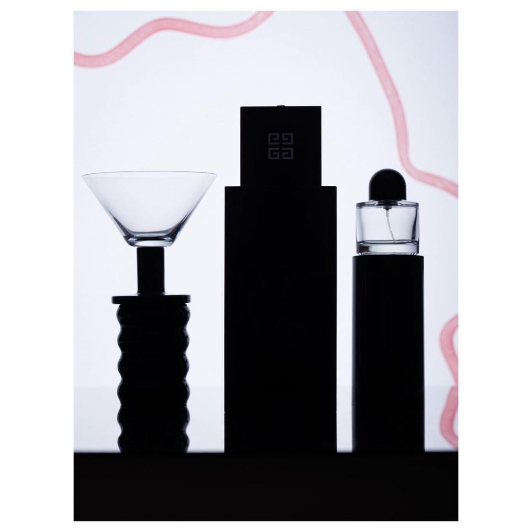 Still life shot of perfume bottles and a cocktail glass featuring sleek, minimalist design against a bright, neutral backdrop with light pink accents.