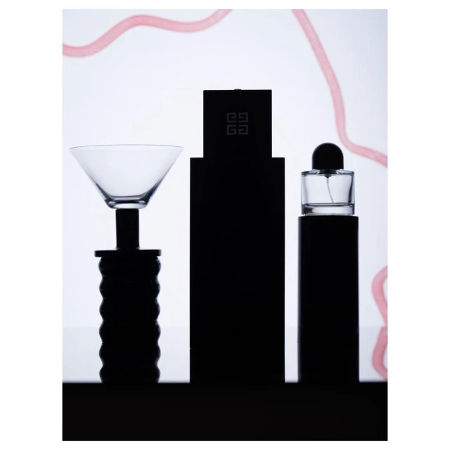 Still life shot of perfume bottles and a cocktail glass featuring sleek, minimalist design against a bright, neutral backdrop with light pink accents.
