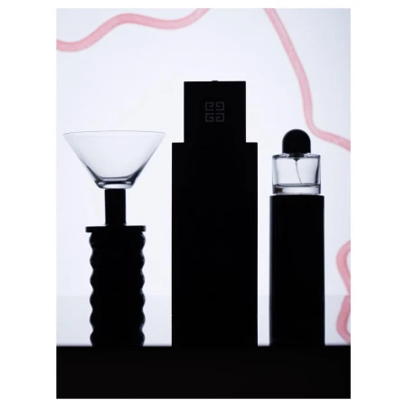 Still life shot of perfume bottles and a cocktail glass featuring sleek, minimalist design against a bright, neutral backdrop with light pink accents.
