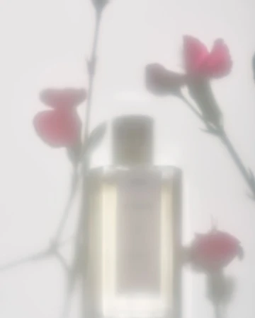 Soft focus studio shot of a perfume bottle with pink flowers in the background creates an elegant, minimalist beauty image.