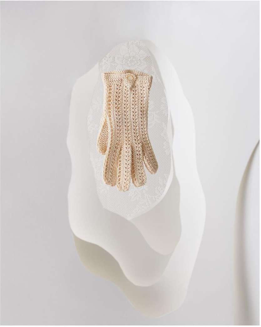 Elegant light beige knitted glove displayed on a textured white surface, fashion still life. Fine textures and soft lighting.