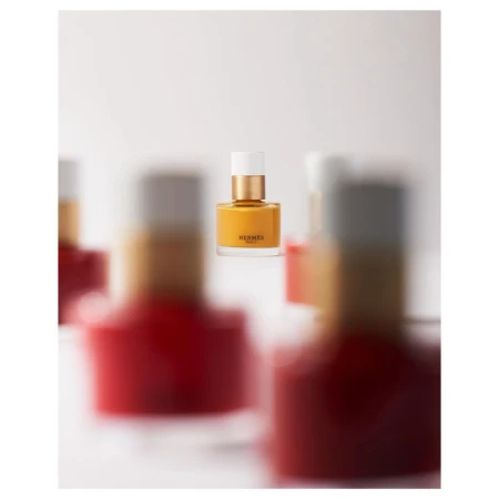 A sharp, centered bottle of yellow nail polish framed by blurred red and white polish bottles in the foreground and background.