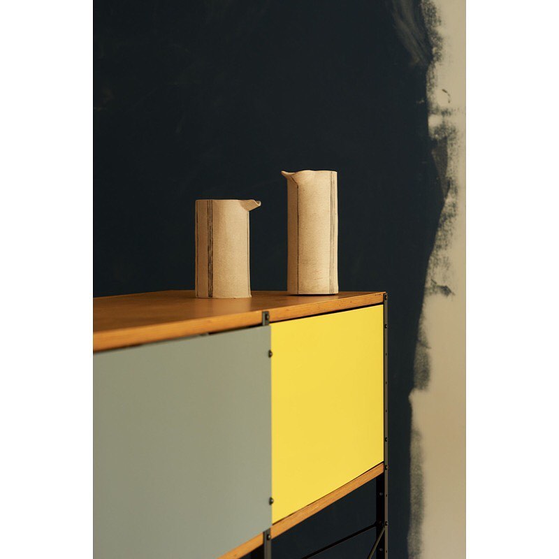 Still life of two ceramic pitchers on a mid-century modern cabinet against a dark blue wall with an unfinished, textured appearance.