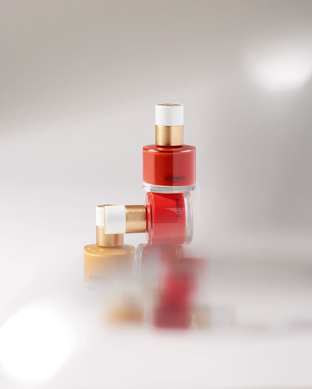 Still life shot of three nail polish bottles stacked against a blurred white background for beauty and cosmetics advertising.