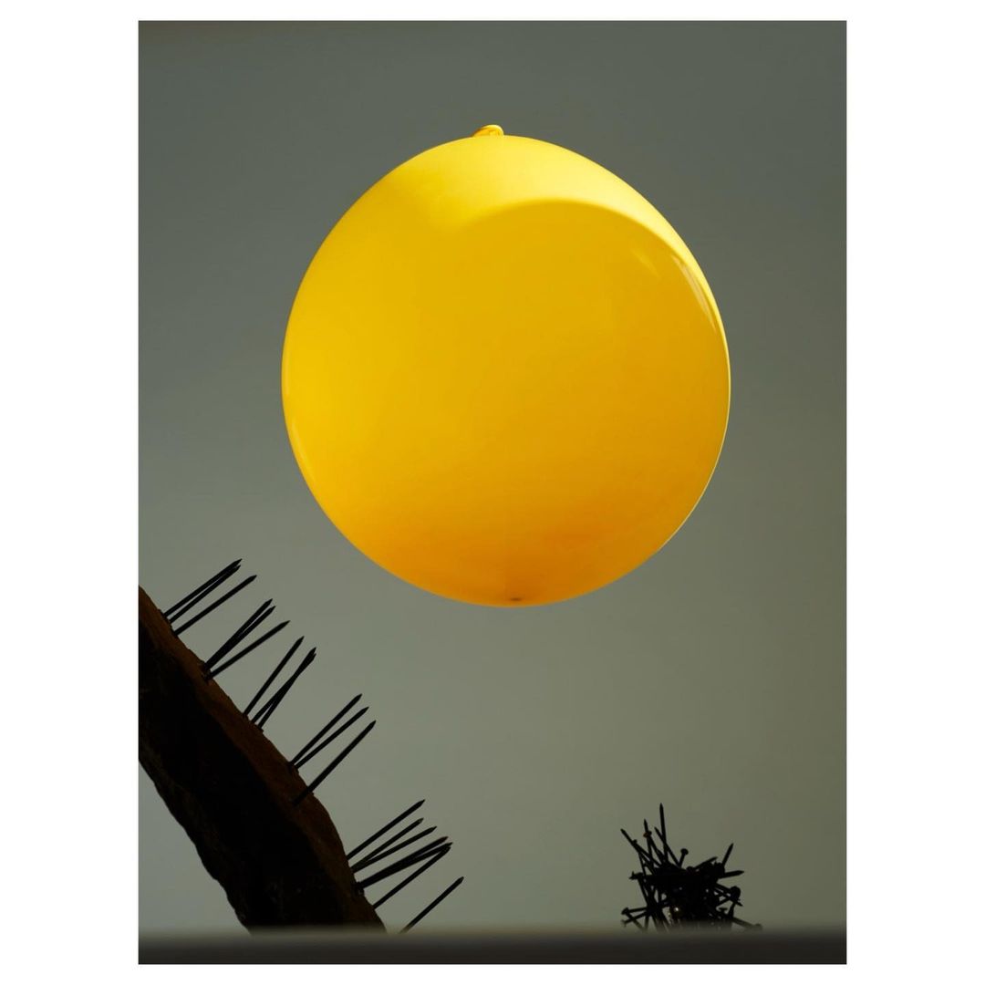 Abstract photography featuring a vibrant yellow balloon against a neutral gray background, complemented by dark, textured objects.