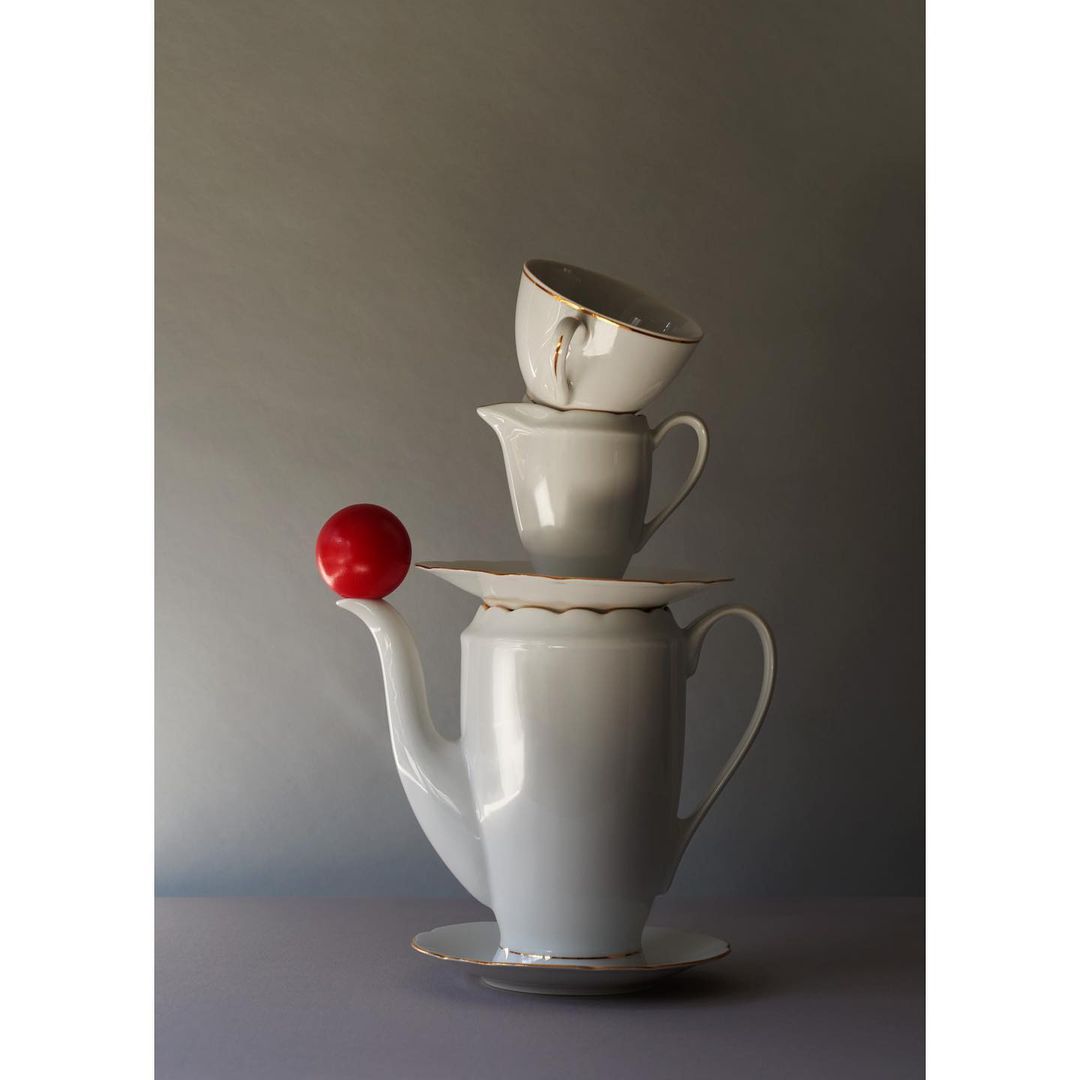 Still life of teaware and a red plum stacked on a gray gradient background in a vertical composition with good lighting and shadows.