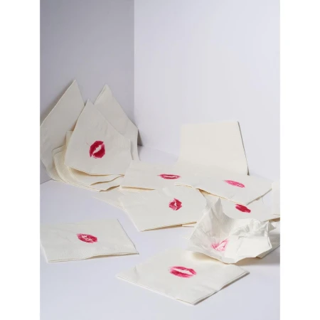 Close-up shot of multiple white napkins scattered around, each bearing a bright red lipstick kiss mark in a clean, white corner setting.