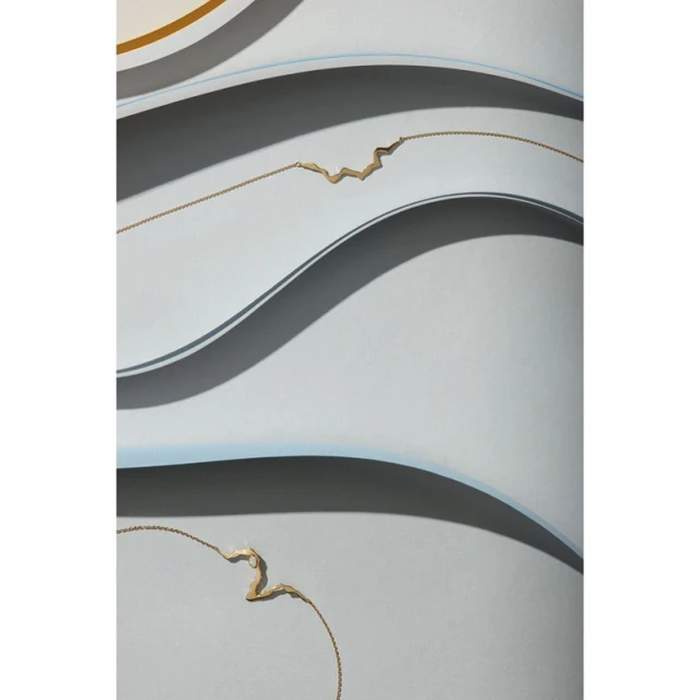 Minimalist art featuring abstract gold necklaces against a muted grey and white background with curving lines and shadows.