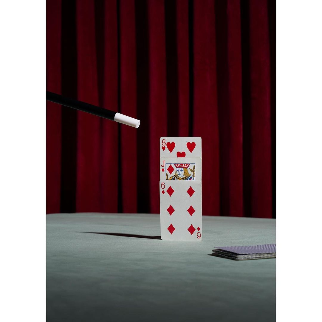 Playing cards, magic wand, and a red curtain create a vintage magic show scene; still life photo for the entertainment industry.