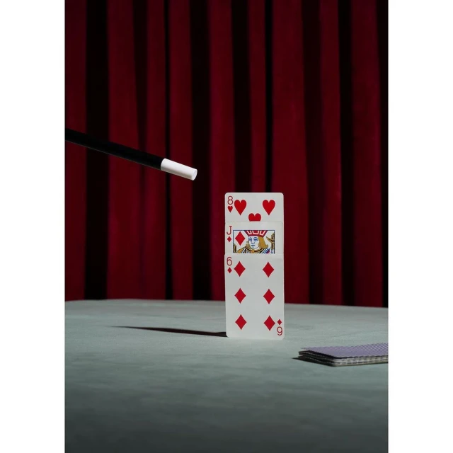 Playing cards, magic wand, and a red curtain create a vintage magic show scene; still life photo for the entertainment industry.