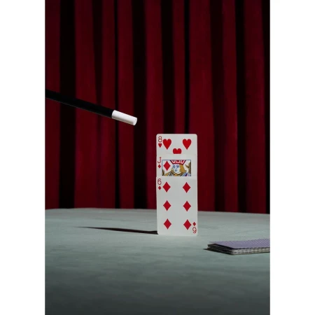Playing cards, magic wand, and a red curtain create a vintage magic show scene; still life photo for the entertainment industry.