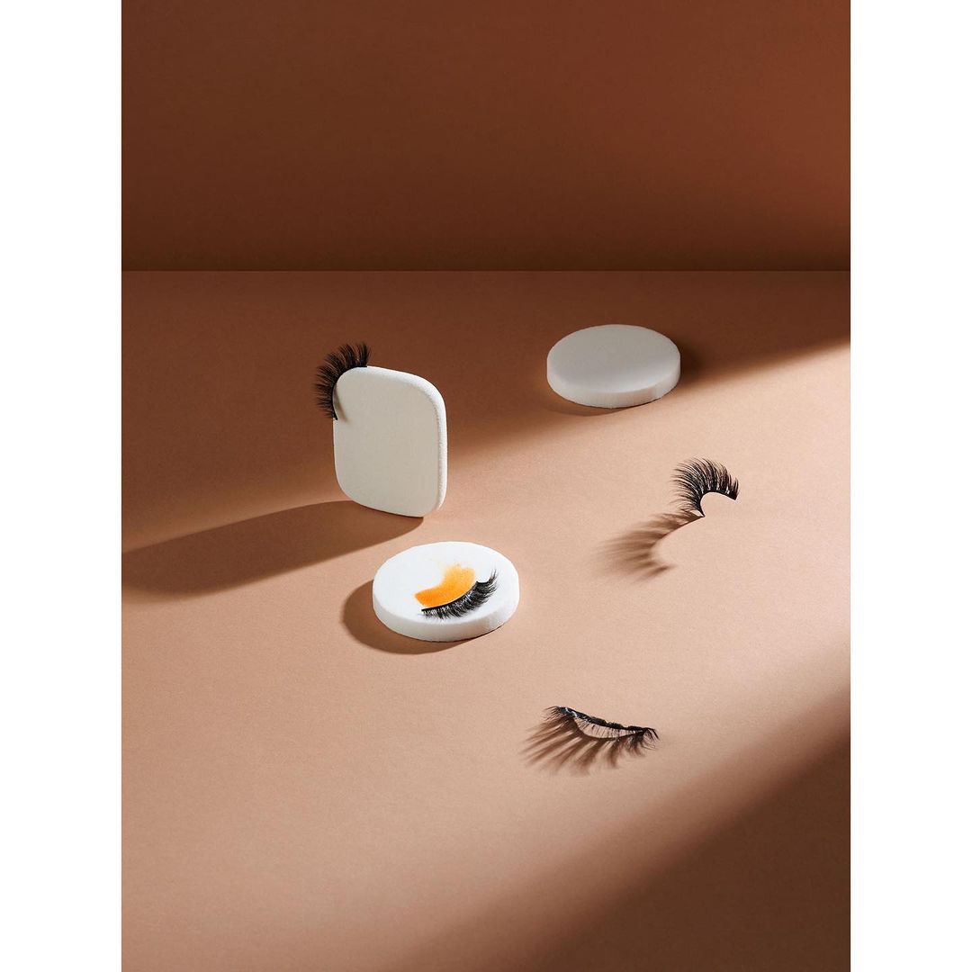 Arrangement of individual false eyelashes on small pedestals against a neutral backdrop, lit to create shadows and highlight the products.