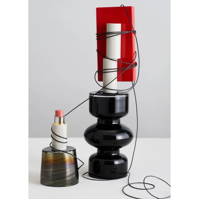 Still life composition featuring a black vase supporting a red block and white cylinder, alongside a copper-toned vase and black cord.