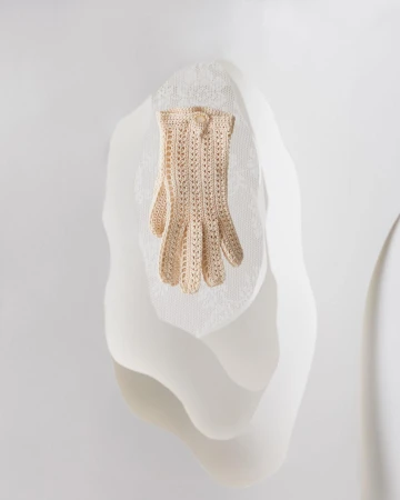 Close-up of a single, cream-colored, openwork crochet glove on a draped, mannequin-like form against a neutral white backdrop.